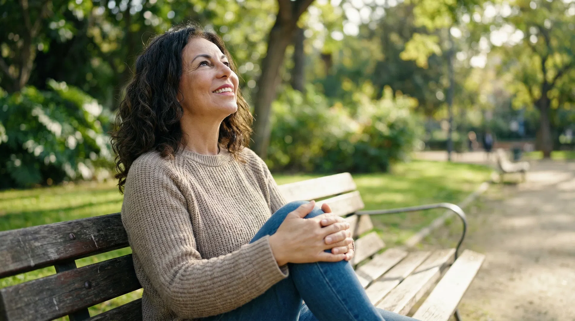 Mujer mexicana de 50 años sentada en un parque, con expresión aliviada, cuidando su rodilla