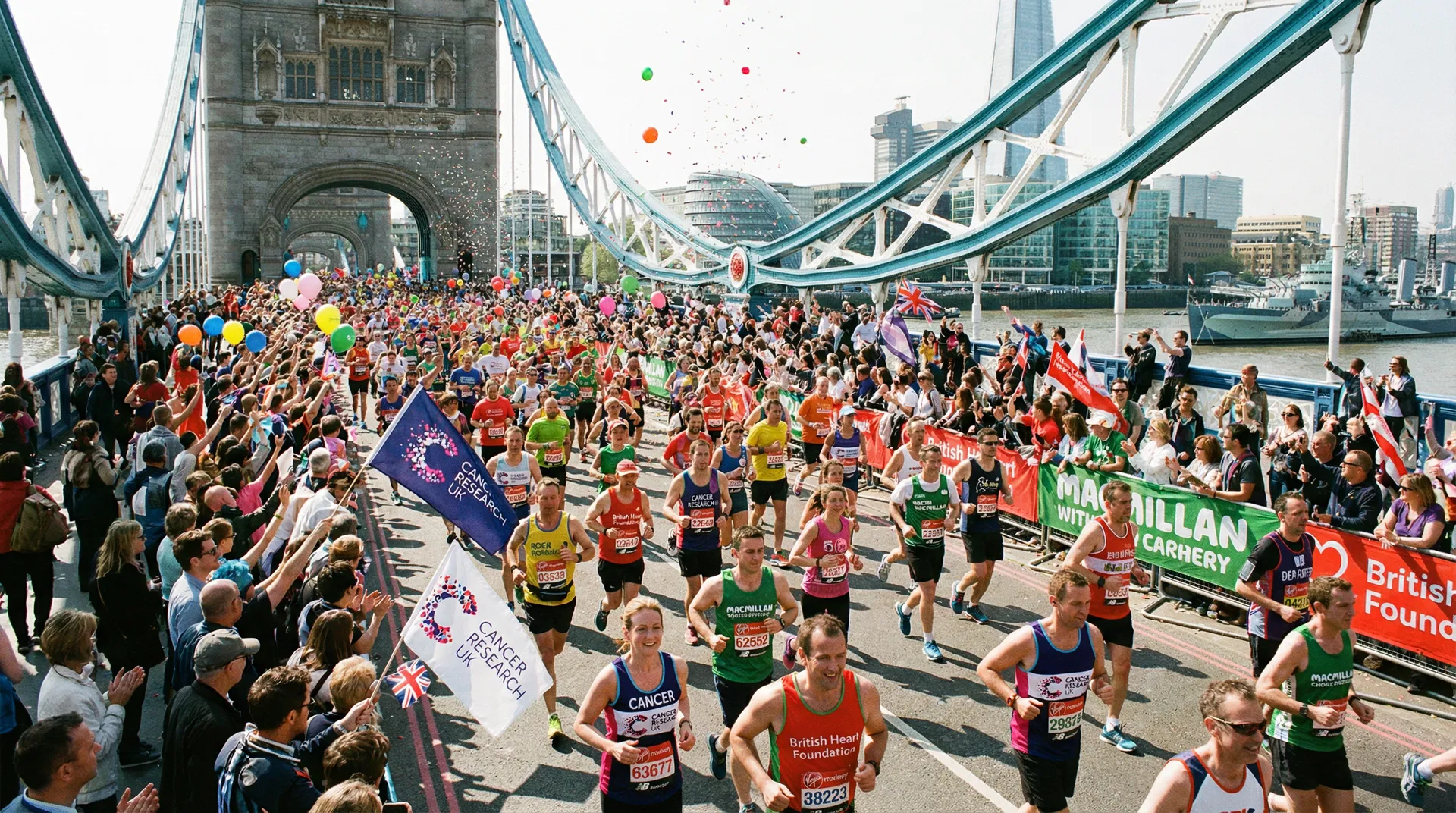 Runners in charity vests crossing Tower Bridge during the London Marathon, crowd cheering