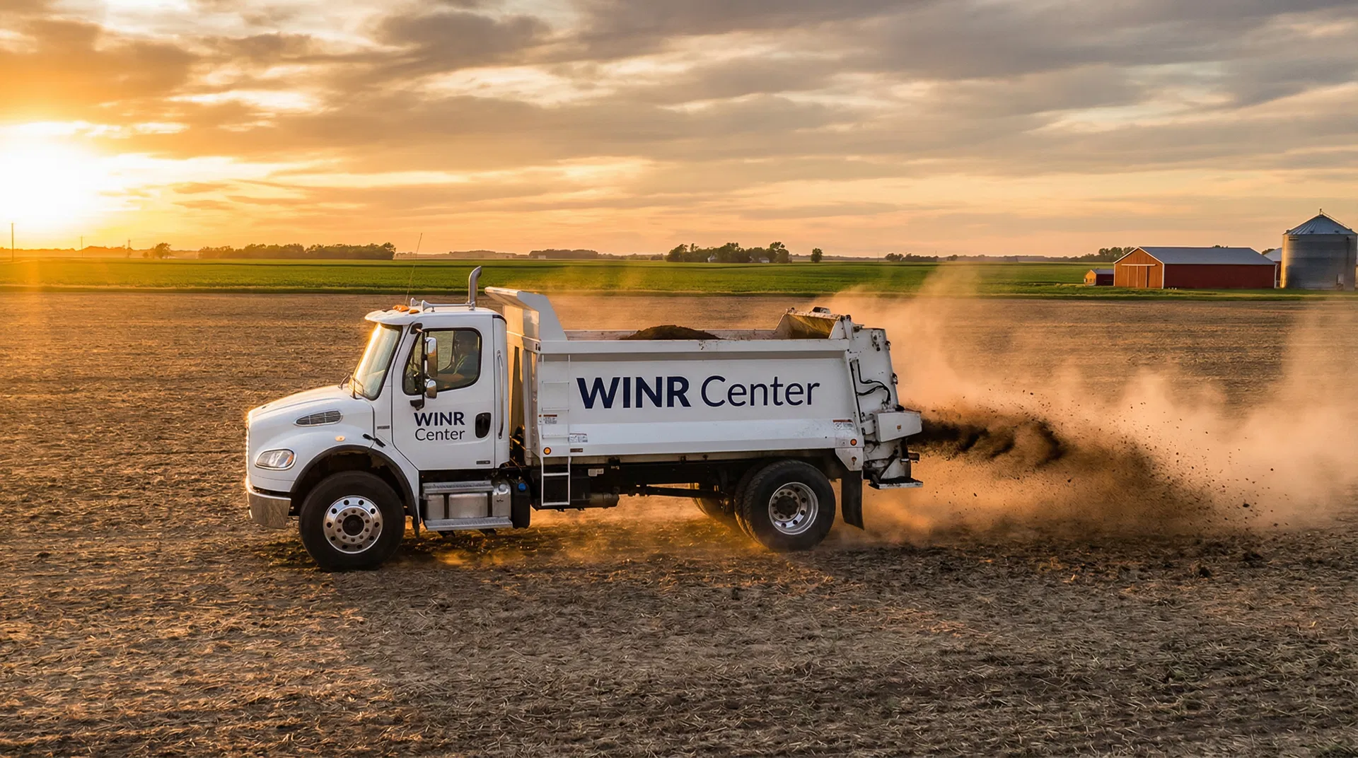 Compost spreader truck applying organic material to an Iowa farm field at golden hour