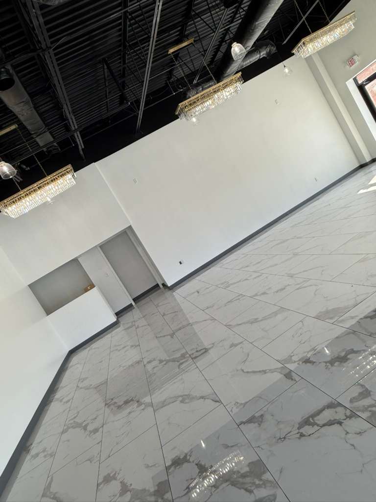 This photo showcases an empty event venue with a sleek, modern design. It features white walls, a black exposed ceiling, elegant crystal chandeliers, and a polished marble-look tiled floor.