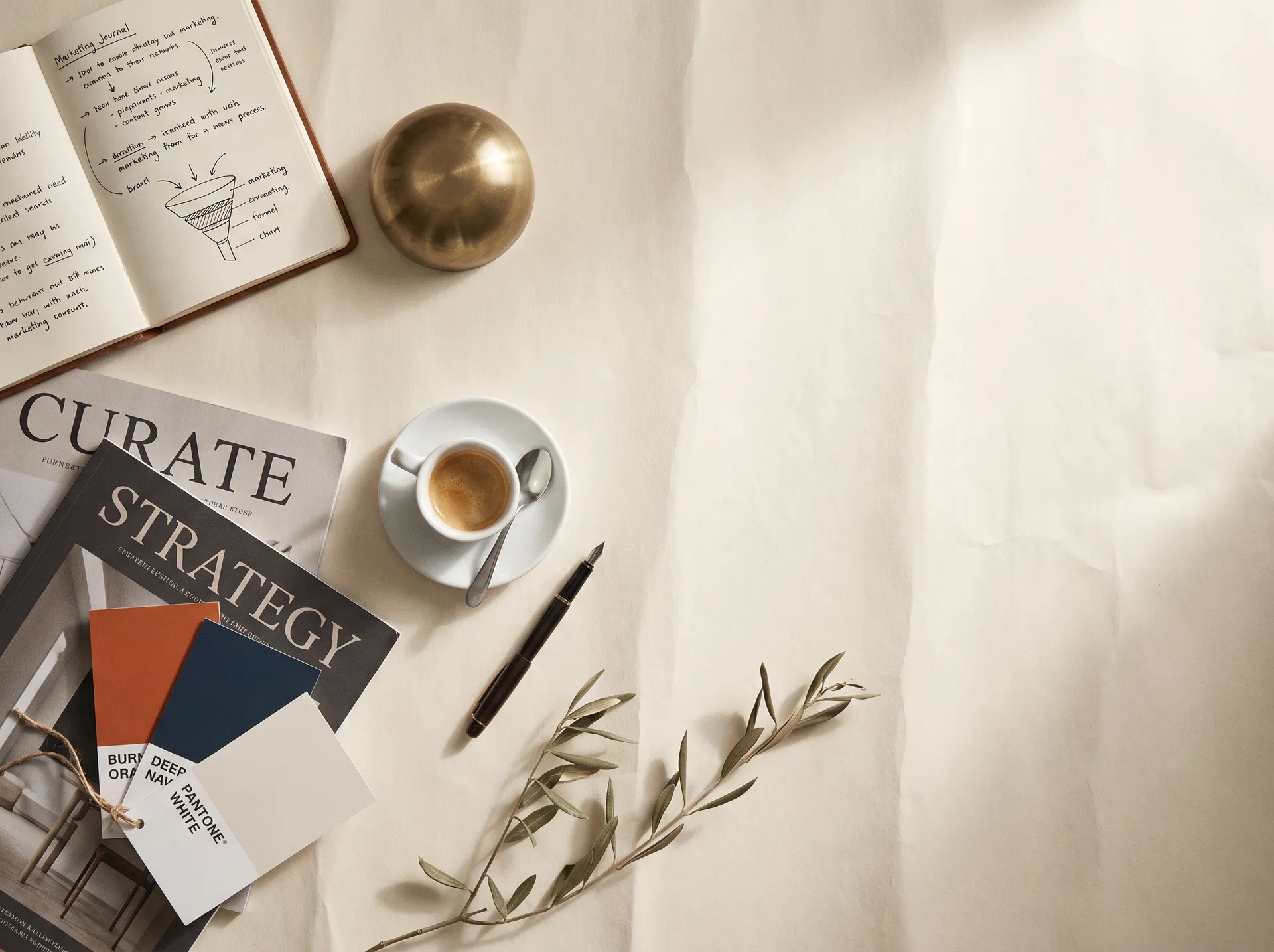 A flat-lay of a notebook with a hand-drawn marketing funnel, magazines, espresso, and Pantone swatches on warm cream paper.