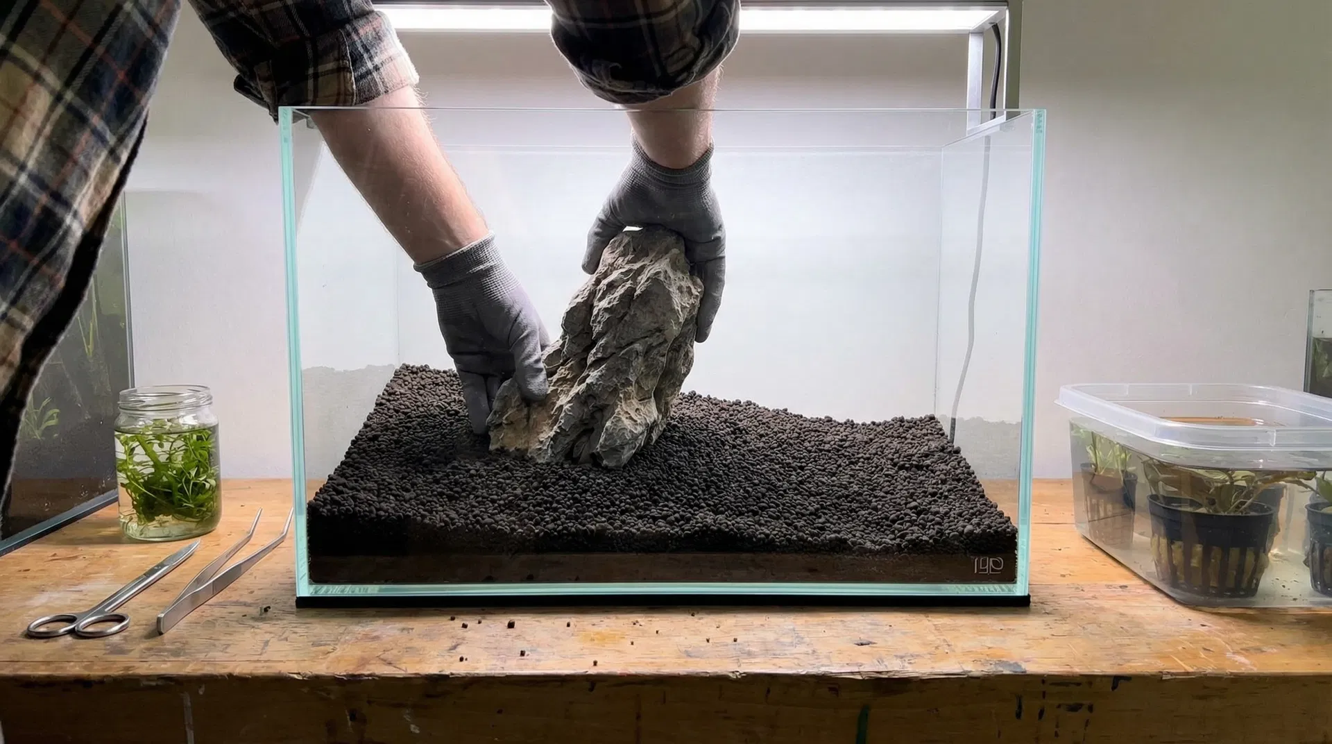 Einrichtungsprozess eines Aquascapes – Hände platzieren Steine im leeren Aquarium