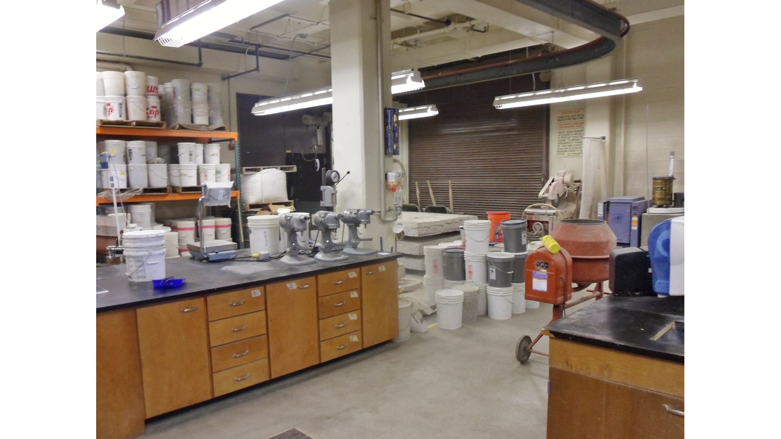 Laboratório de engenharia civil com equipamentos, recipientes e amostras de concreto para ensaios