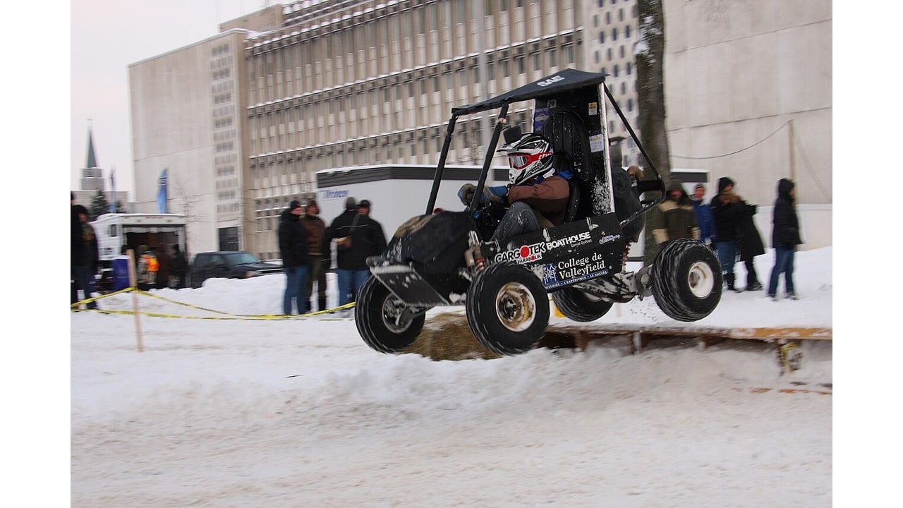 Veículo monoposto de Baja SAE saltando sobre uma pista nevada diante de espectadores.