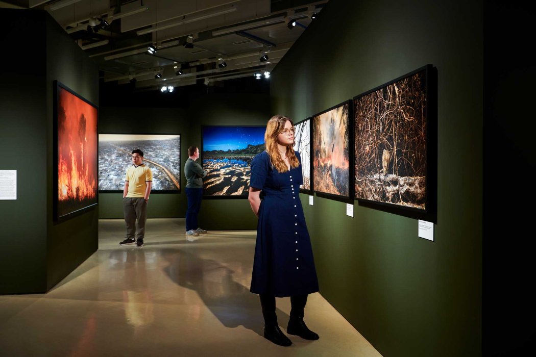 Pessoas observando fotografias de paisagens e animais em uma exposição fotográfica sobre o Pantanal