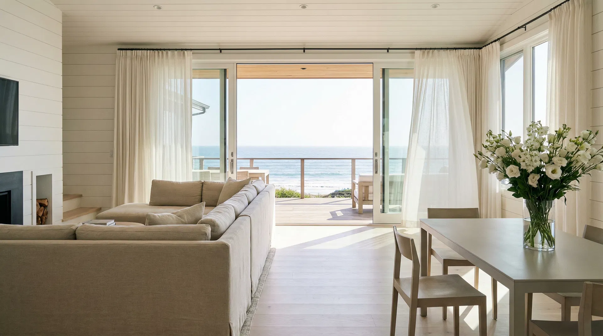 Immaculately clean Stinson Beach vacation home interior with bleached wood floors, white shiplap walls, and floor-to-ceiling sliding glass doors open to a private deck overlooking the Pacific Ocean