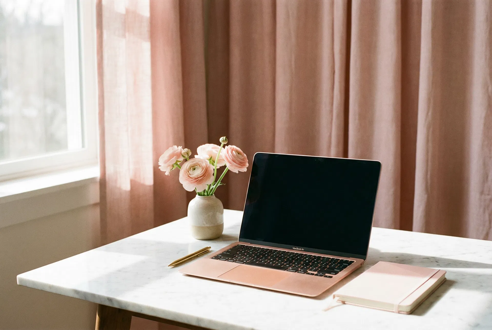 Rose gold laptop on marble desk with pink ranunculus flowers and gold pen — Glow Goddess LLC professional workspace in Waveland MS