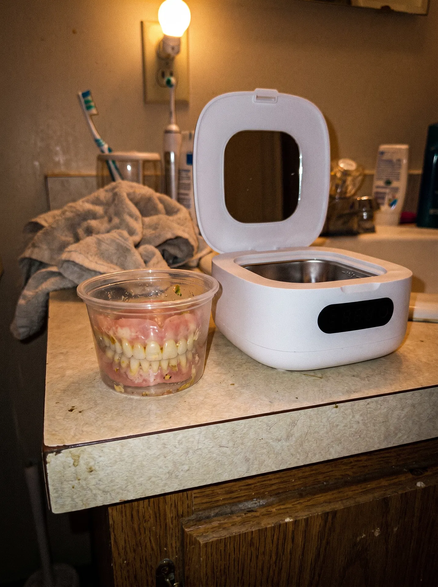 Smartphone-style photo of used dentures in a cup beside Klenopod before cleaning
