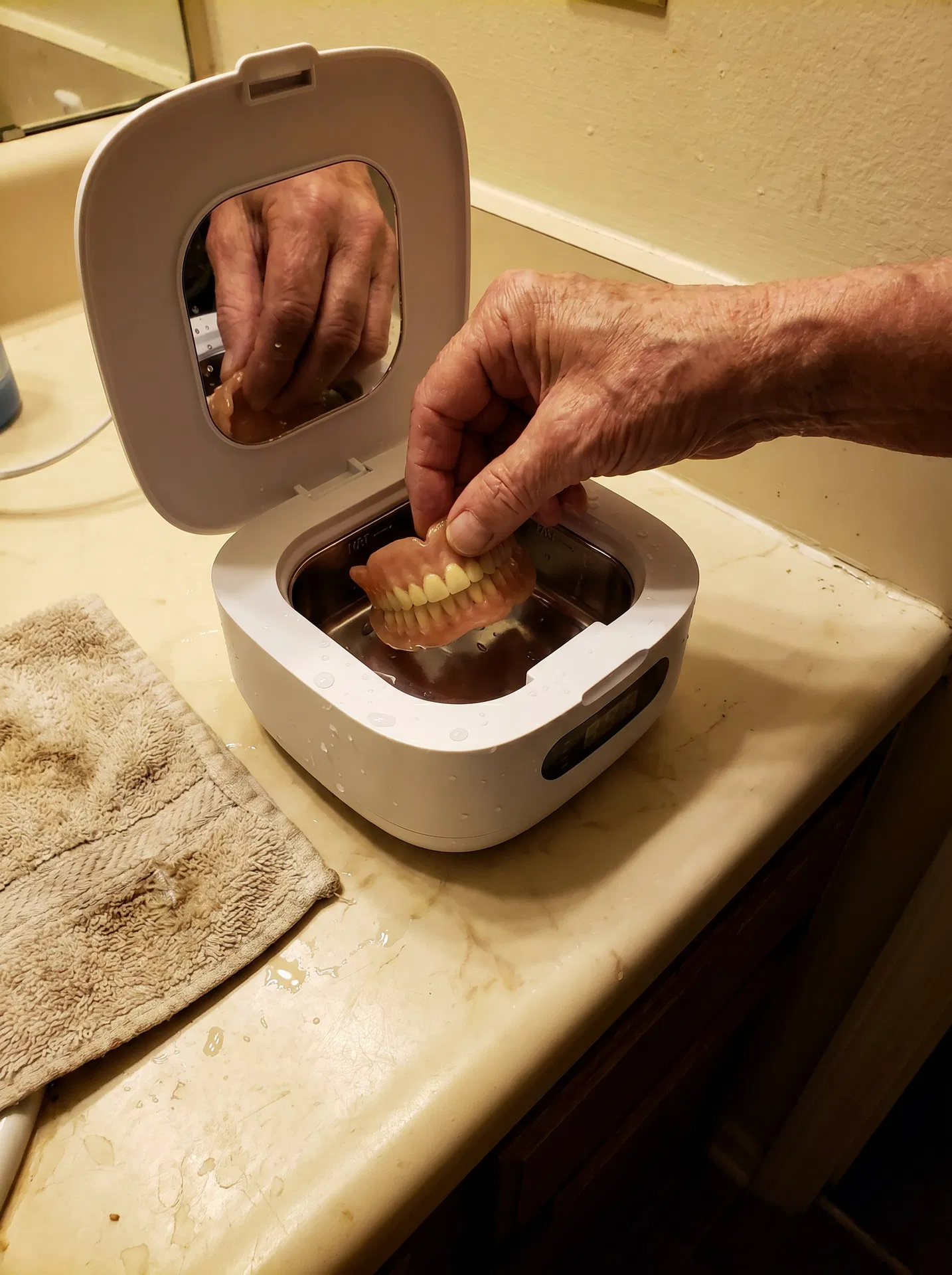 Older hands placing dentures into an open Klenopod cleaning pod