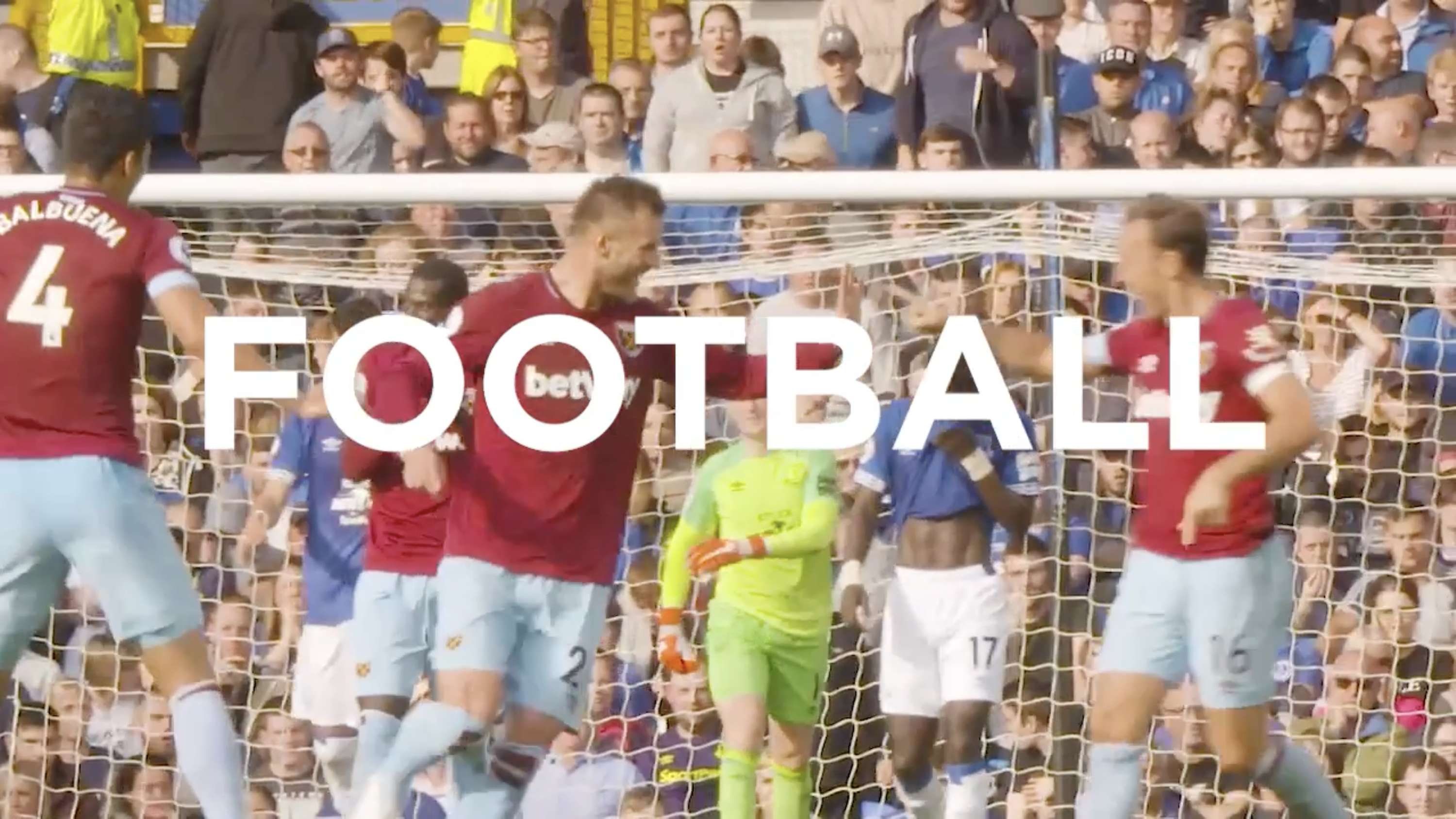 Two excited kids in West Ham United t-shirts cheer enthusiastically at a sports event.