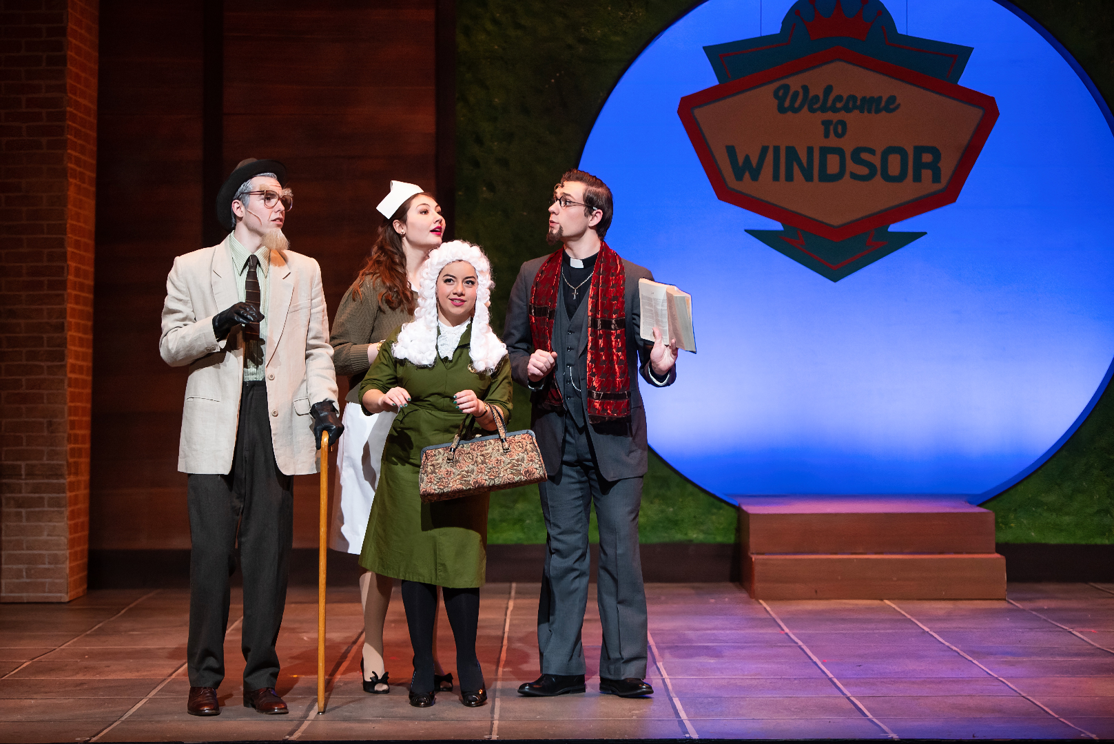 The Merry Wives of Windsor - Scenic design by Brandon PT Davis. Vibrant Elizabethan village square, timber-framed houses, market stalls, colorful banners, bright sky.