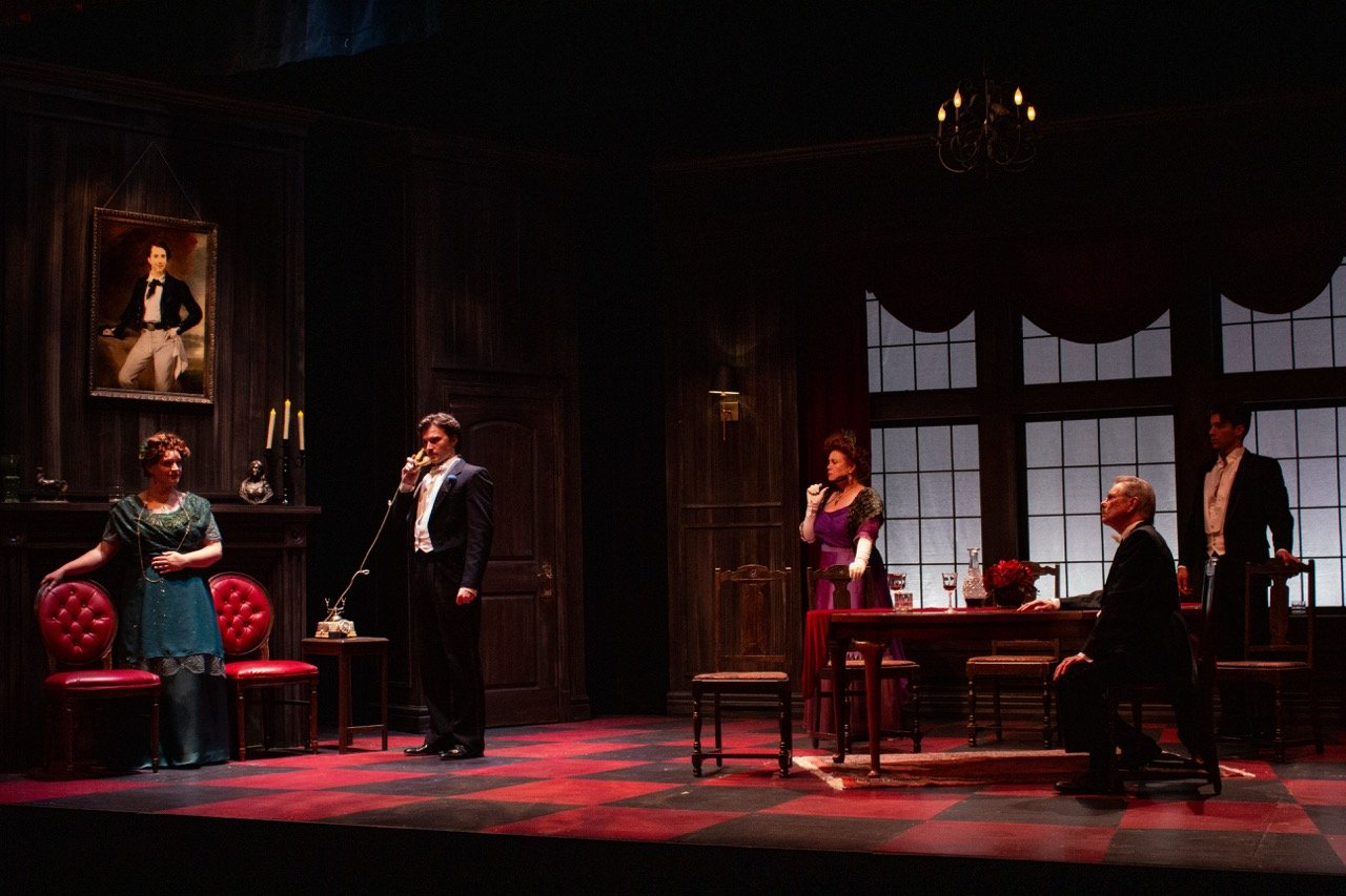 An Inspector Calls - Scenic design by Brandon PT Davis. A Victorian dining room set with dark wood, a long table, and dim, oppressive lighting, conveying a tense and somber mood.