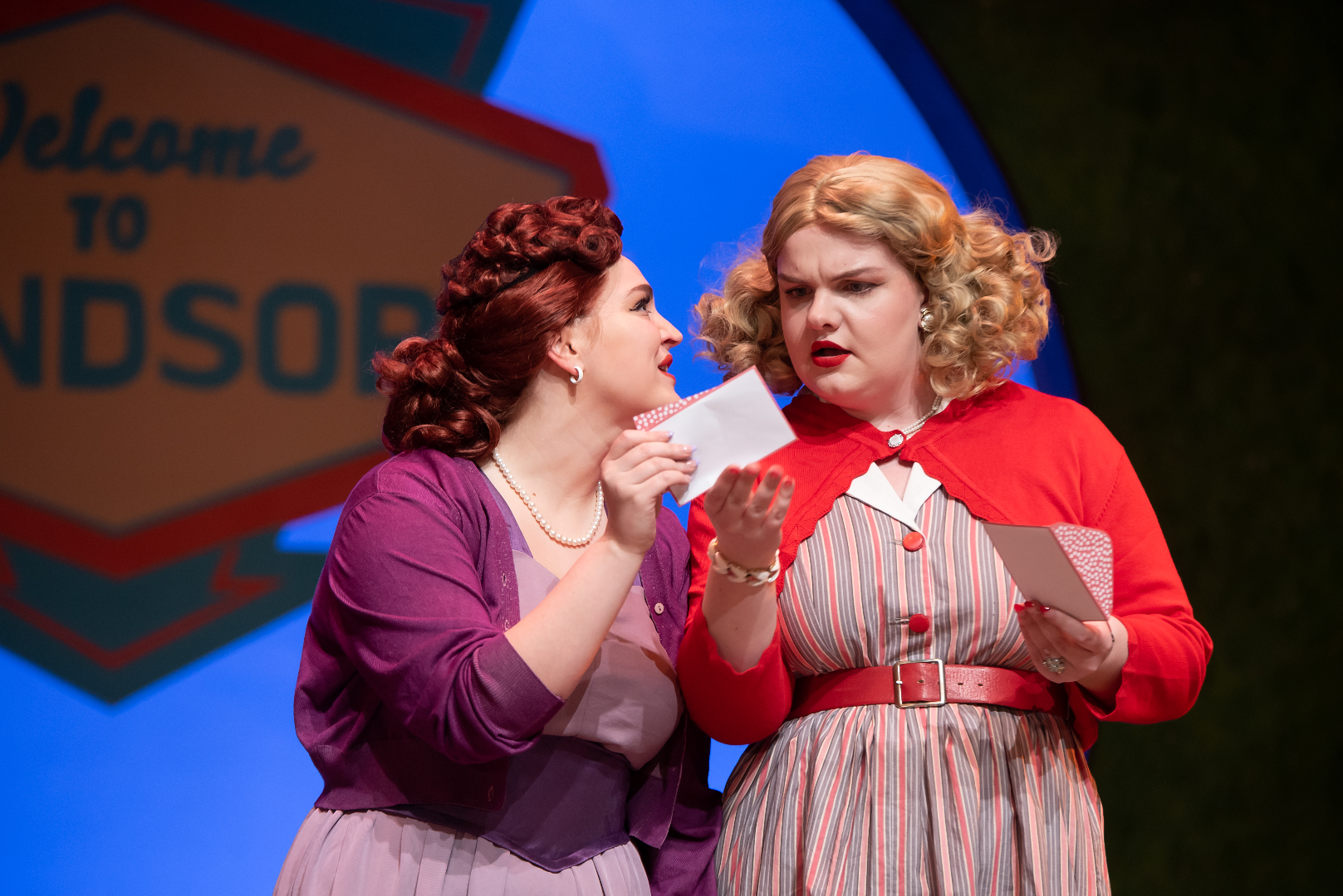 The Merry Wives of Windsor - Scenic design by Brandon PT Davis. A lively Elizabethan village square with timber-framed houses and warm lighting, reflecting the play's comedic spirit.