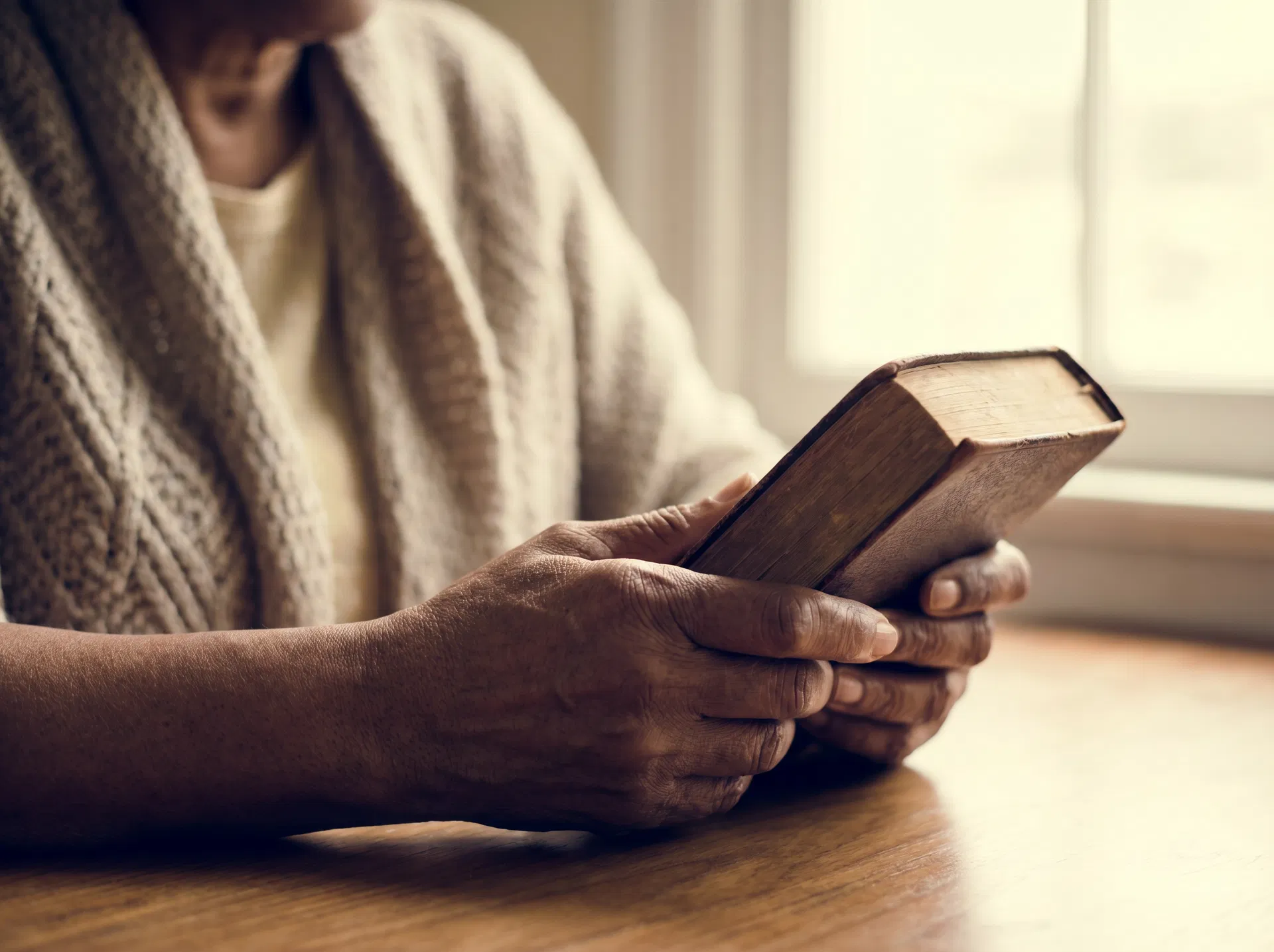 Hands holding a Bible in warm window light