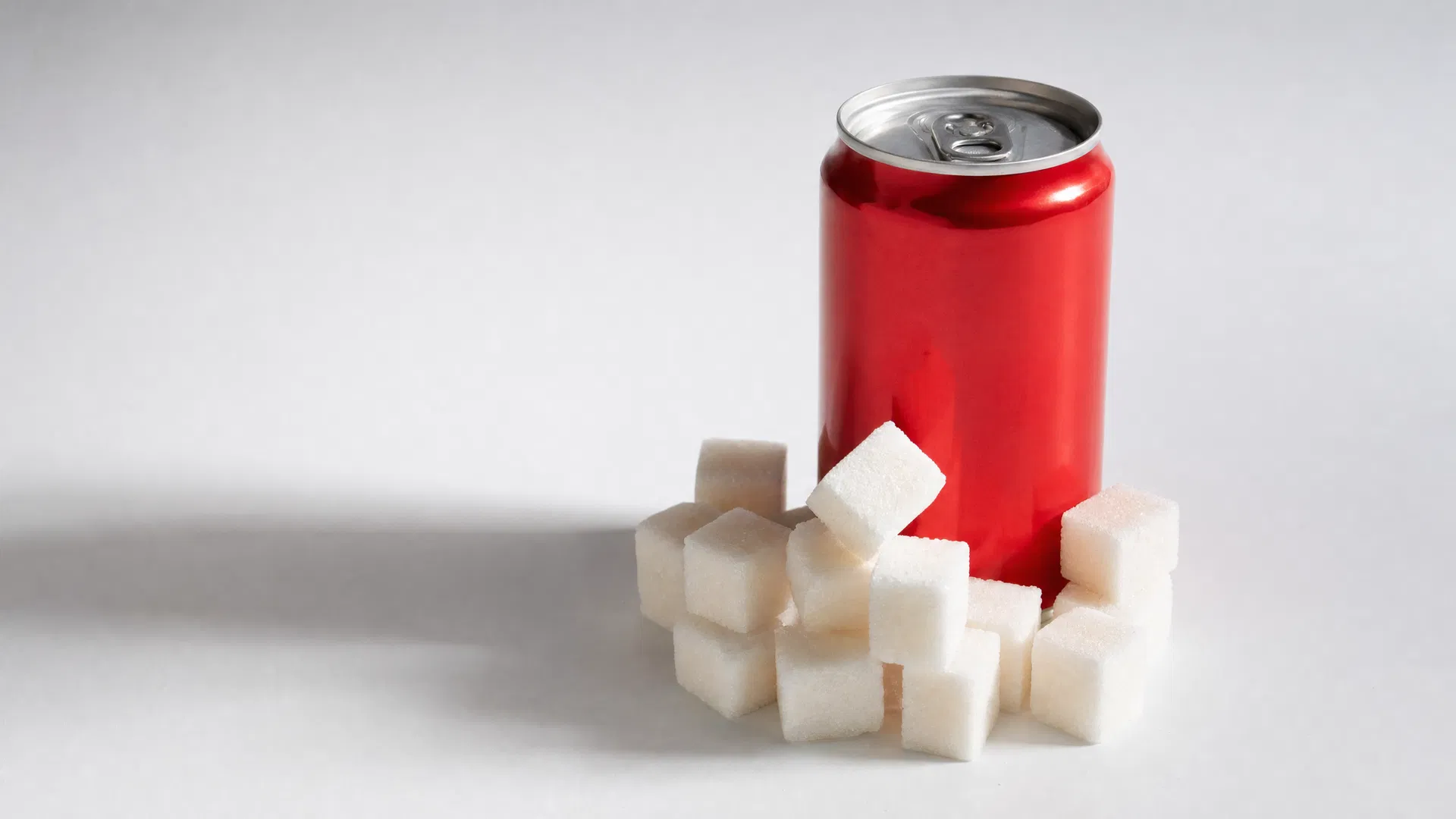 A pink soda can surrounded by white sugar cubes, illustrating the hidden sugar content in sugary beverages marketed to children