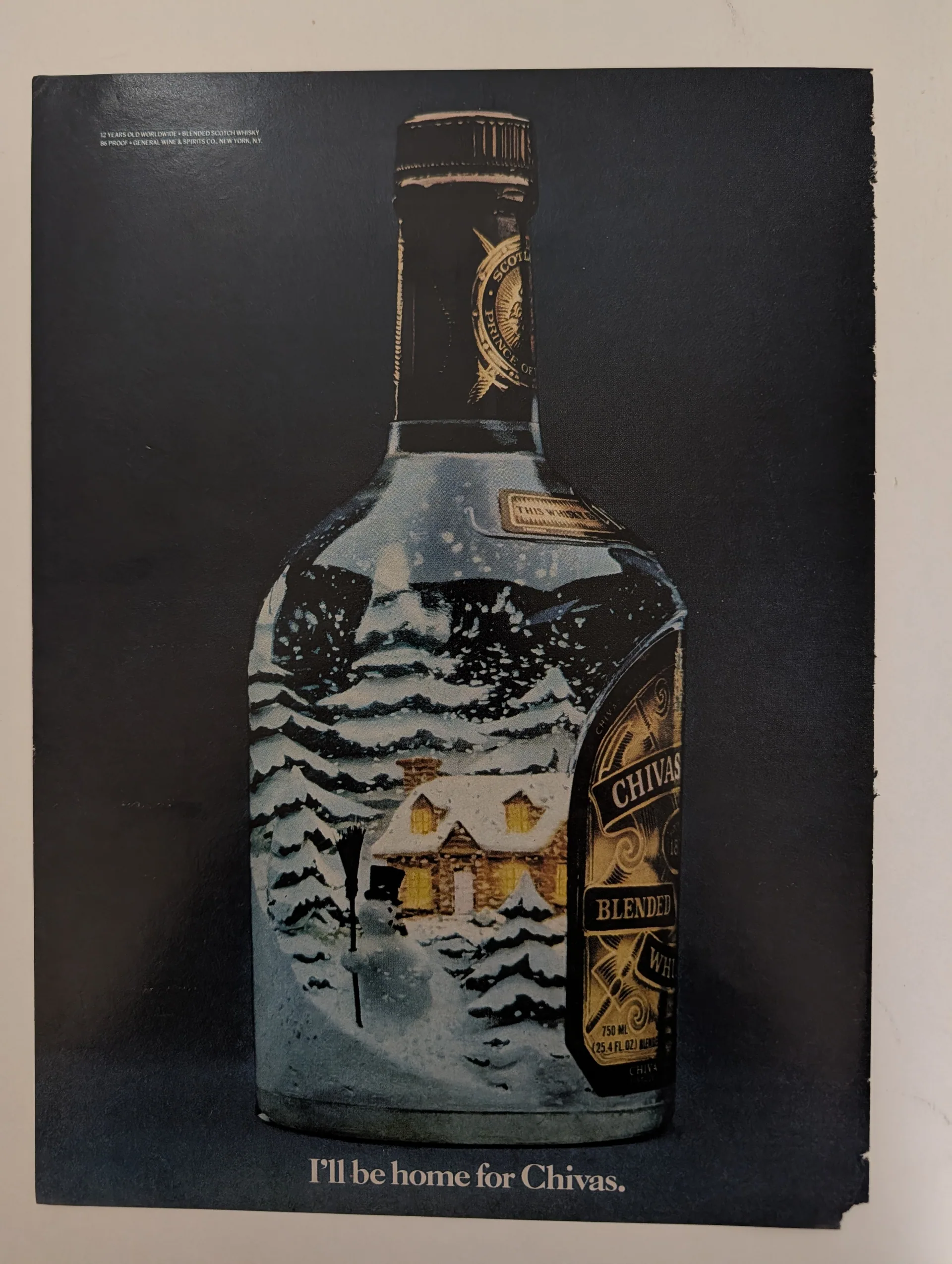 Full-page color print advertisement for Chivas Regal 12 blended Scotch whisky: a bottle bearing a painted winter Christmas scene — snow-covered cabin, snowman, pine trees — against a dark background, 