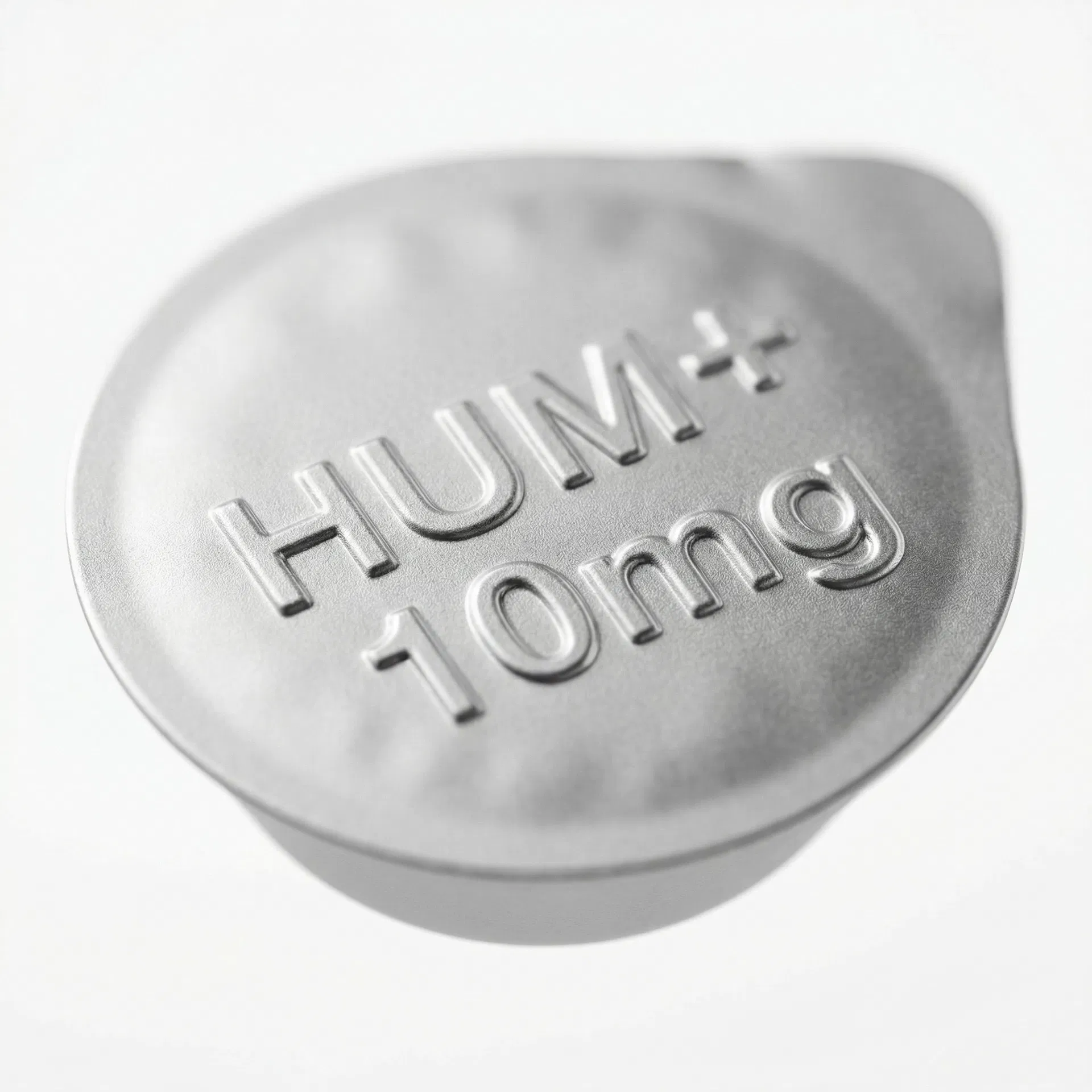 HUM+ foil seal close-up — embossed dose marking on matte silver pharmaceutical foil
