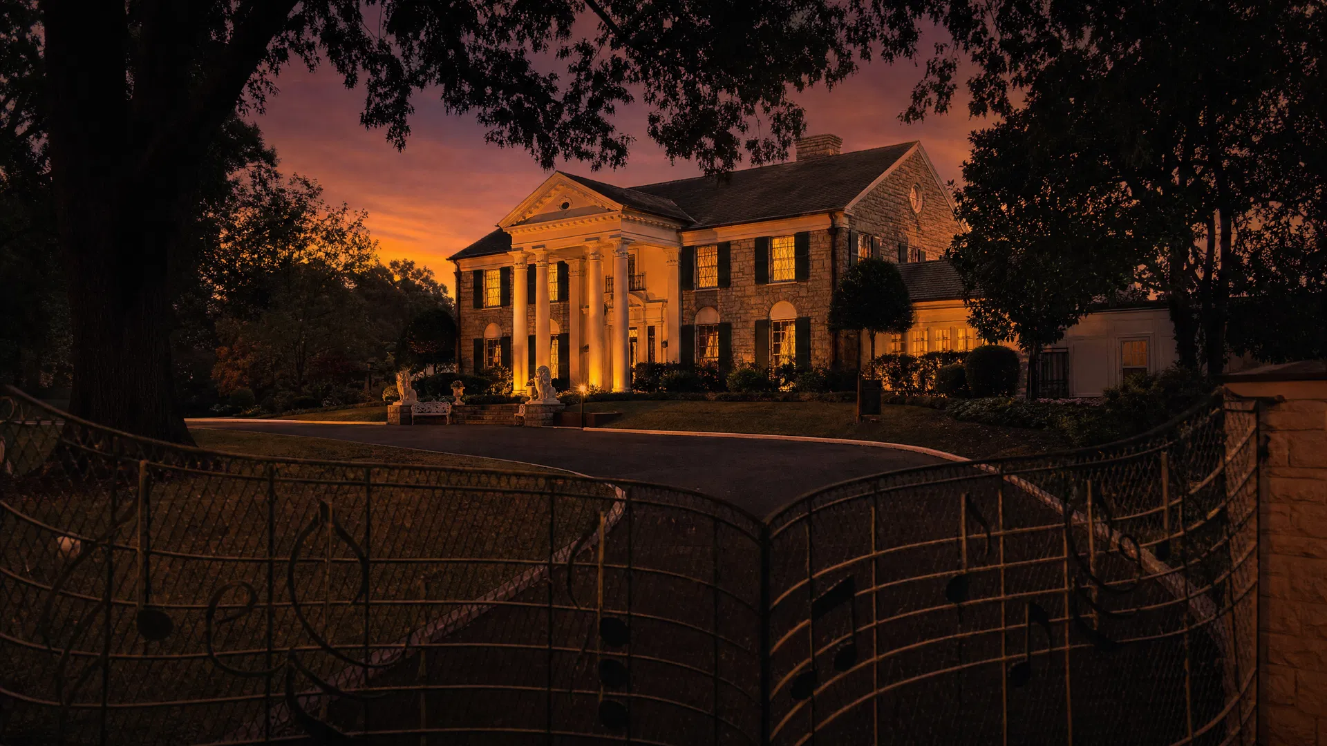 Graceland mansion at dusk, warm golden light from windows against a purple twilight sky