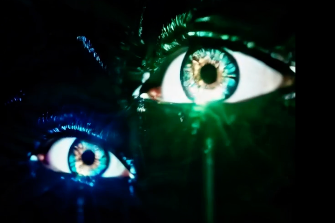 Two luminous eyes glowing teal and green in near-total darkness, fractured and overlapping