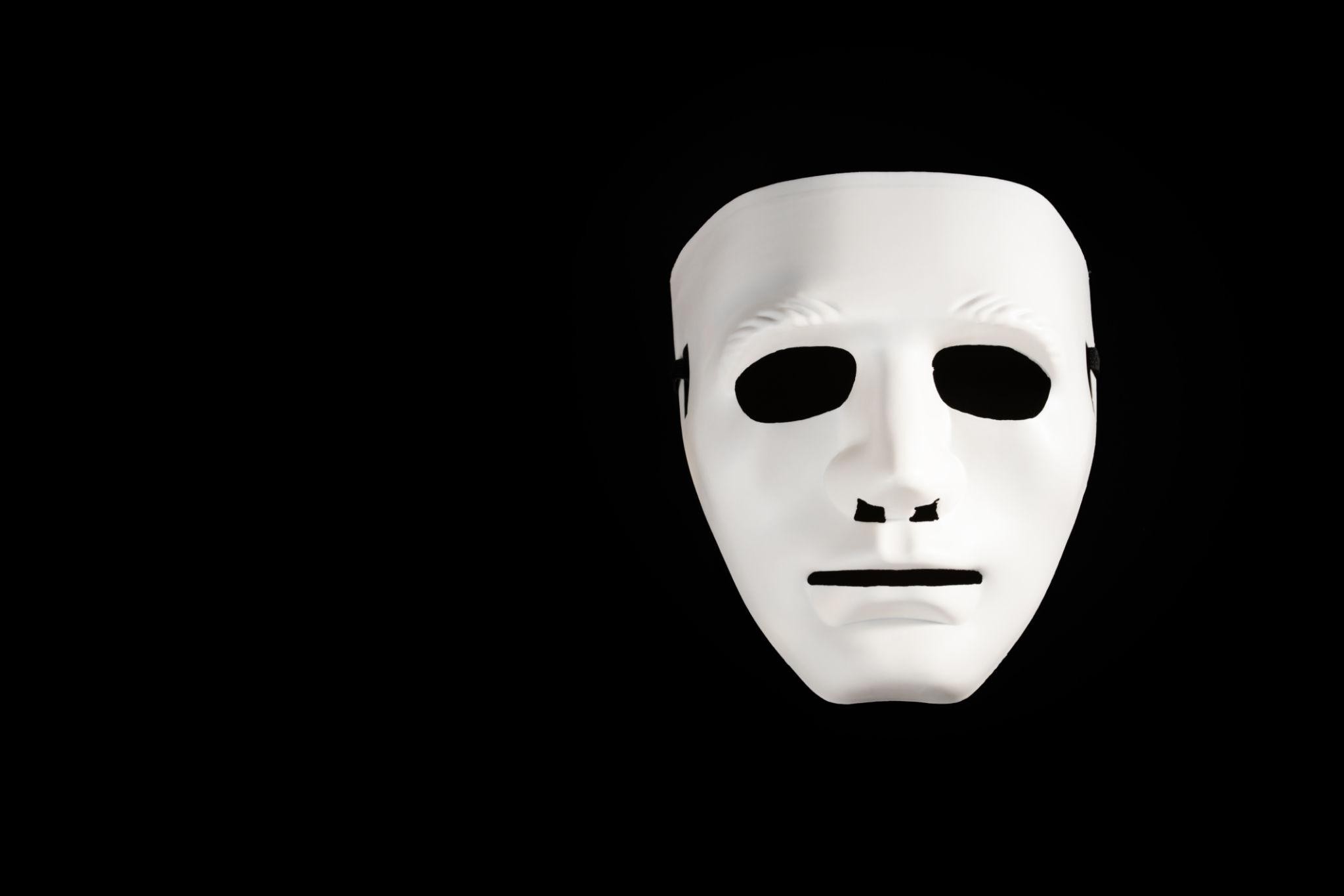 A plain white theatrical mask floating against a solid black background