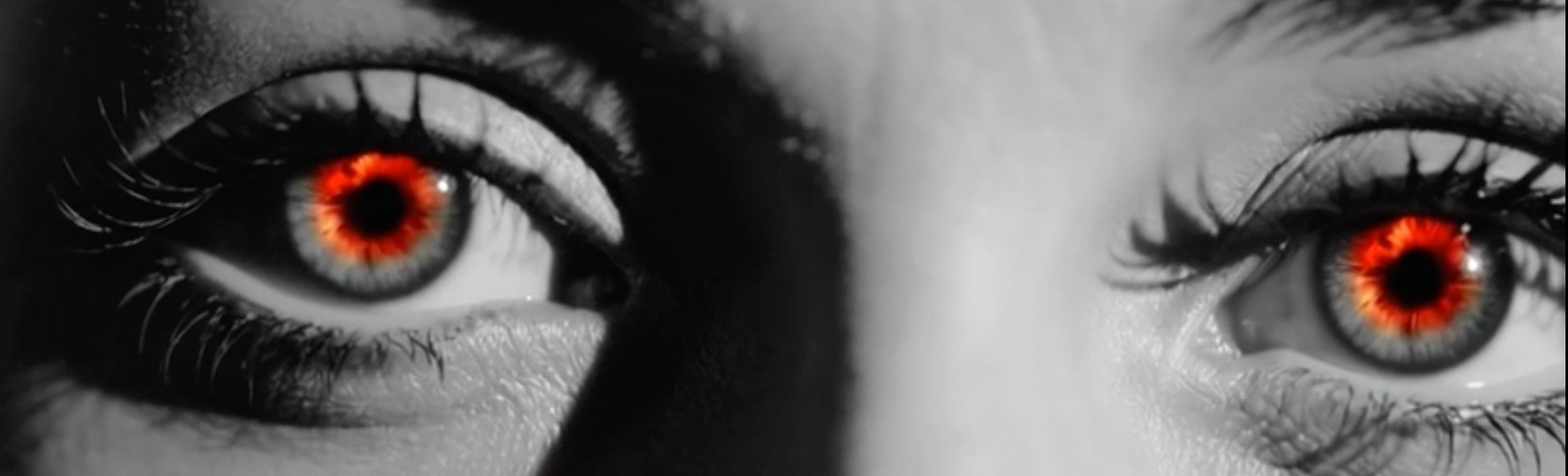 Two close-up eyes with vivid red irises against a black-and-white face, unsettling and intense