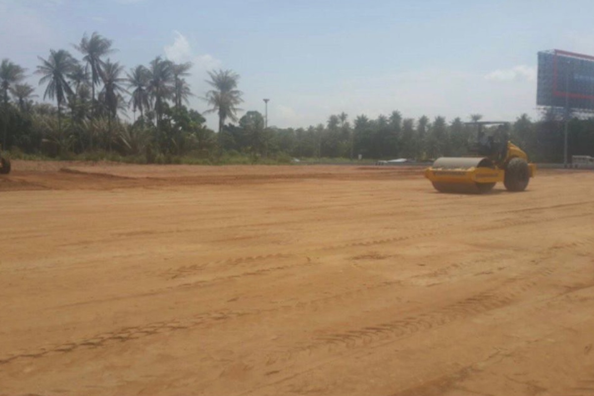 Land for Sale in Nong Pla Lai, large cleared dirt plot with a yellow road roller, palm trees, and a billboard.
