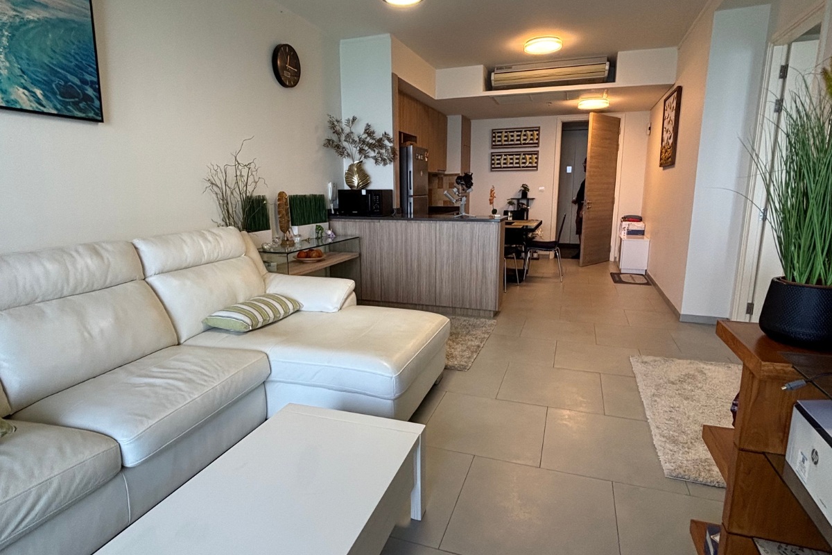 1 Bedroom Condo for Sale at Zire Wongamat living room with white sectional sofa, leading to kitchen and hallway.