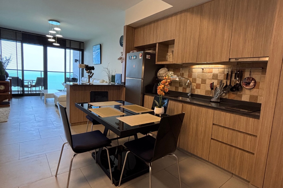 1 Bedroom Condo for Sale at Zire Wongamat kitchen with wooden cabinets, dining table, and living area view.