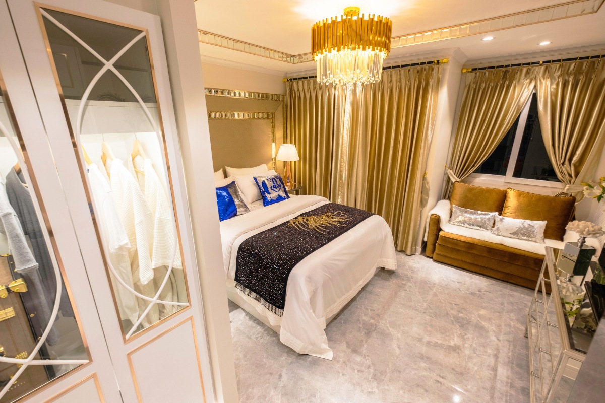 Studio Condo for Sale at Seven Seas Le Carnival: Bedroom with bed, gold curtains, sofa, and open closet with robes.