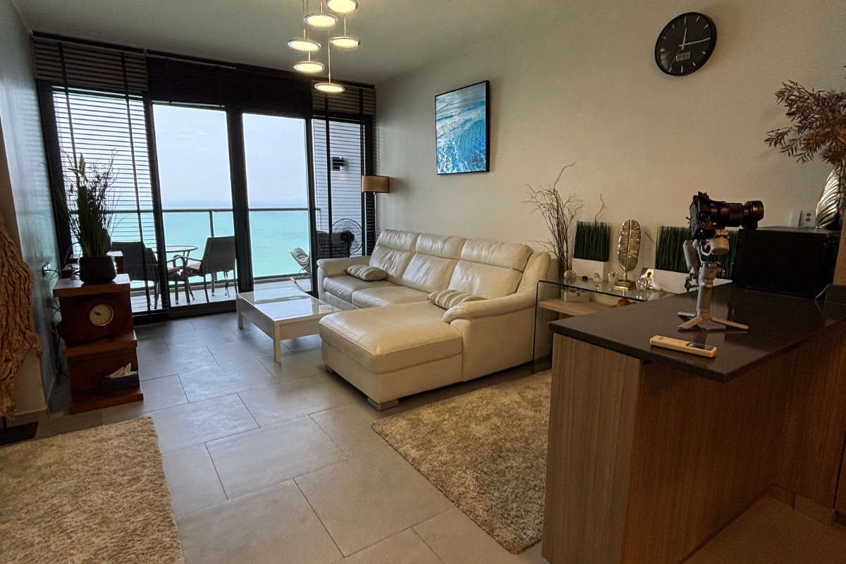 1 Bedroom Condo for Sale at Zire Wongamat living room with white sectional sofa and balcony with ocean view.