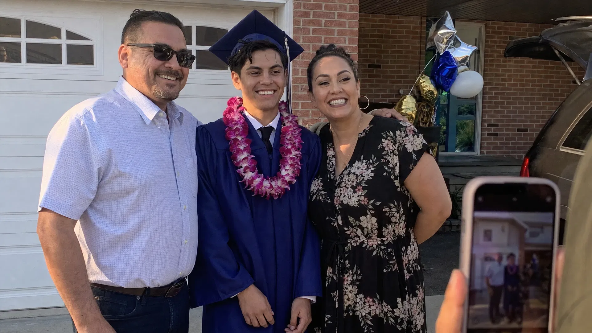 Family taking a photo with their graduate in cap and gown in the driveway after the ceremony