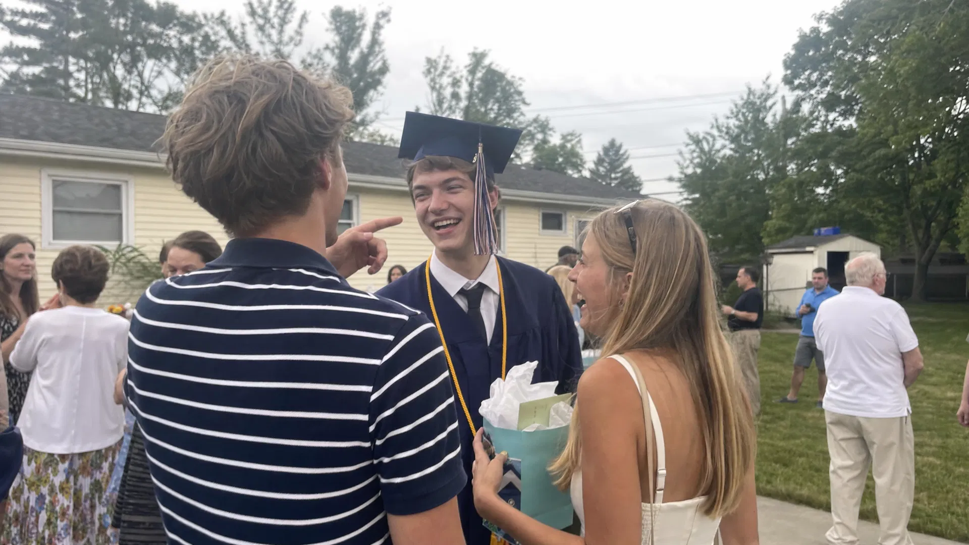 Graduate in cap and gown laughing with friends outside the house after graduation