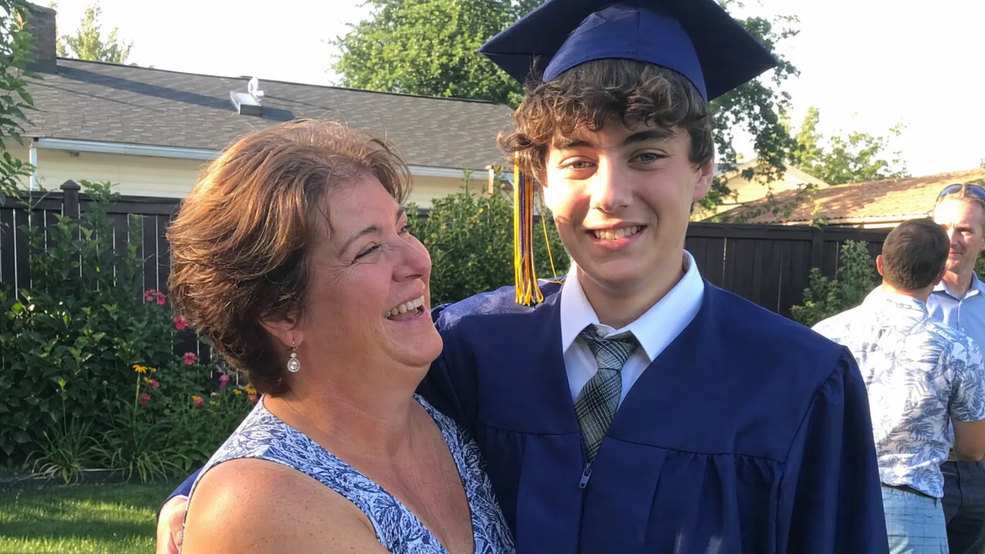 Mom laughing with her son in graduation cap and gown in the backyard after his high school graduation