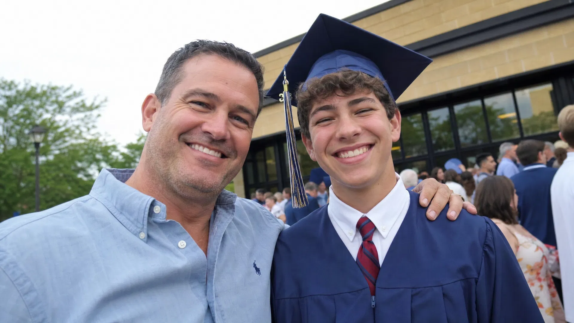 Uncle with his arm around his nephew in graduation cap and gown outside the school