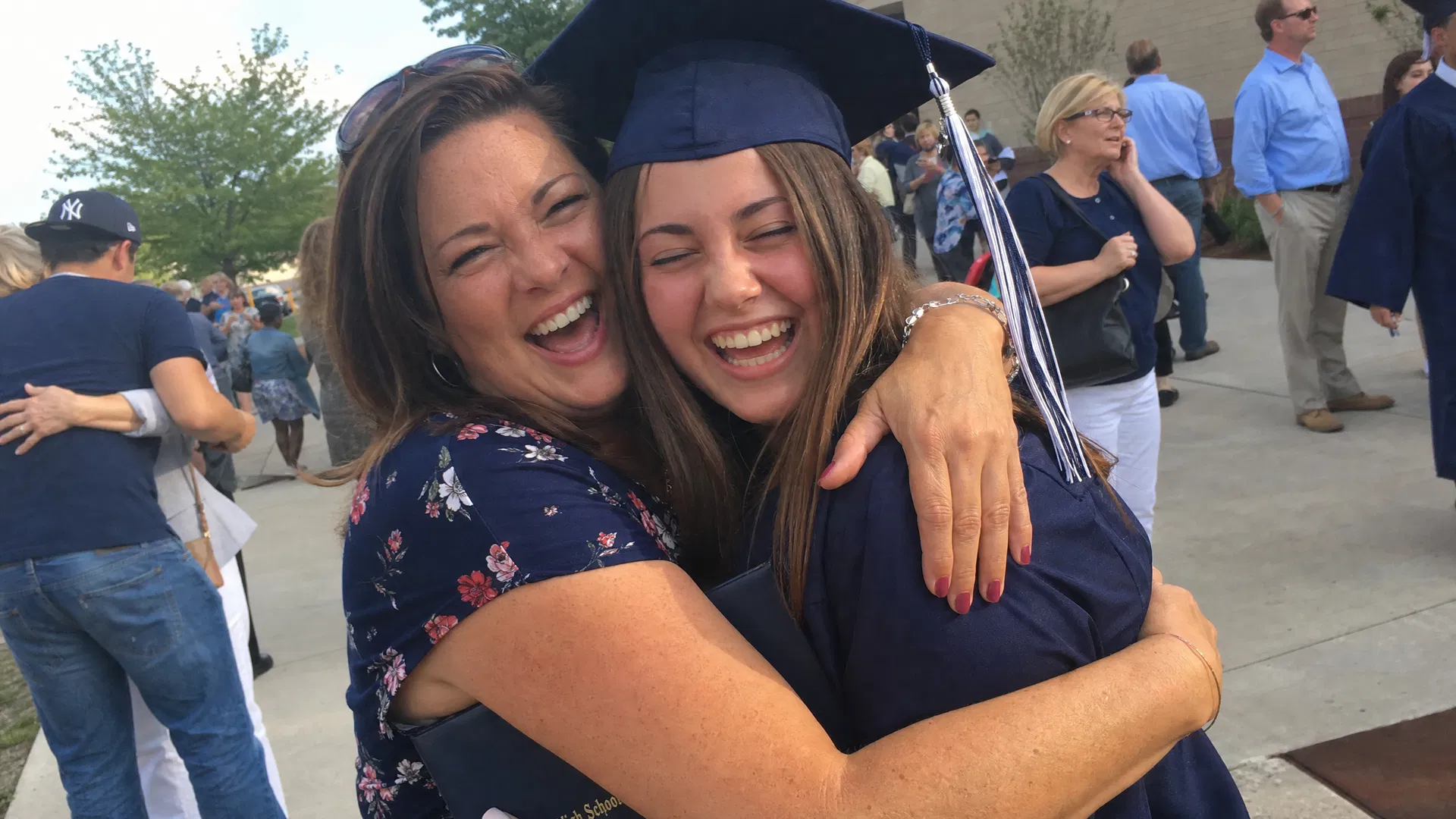 Aunt hugging her niece in graduation cap and gown after the ceremony, both laughing