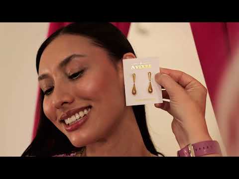 Smiling woman looking at golden teardrop earrings from AVIXEE held up next to her ear, showcasing boutique jewelry in Charlotte NC