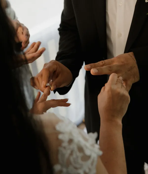 Close-up of a groom's hands placing a diamond wedding ring on the bride's finger during a wedding ceremony.