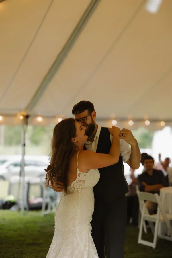 Happy bride and groom dancing closely at their outdoor wedding reception under a tent with string lights.