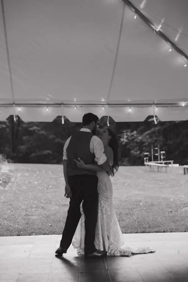 Black and white photo of a bride and groom embracing and looking at each other during their first dance under a wedding tent.