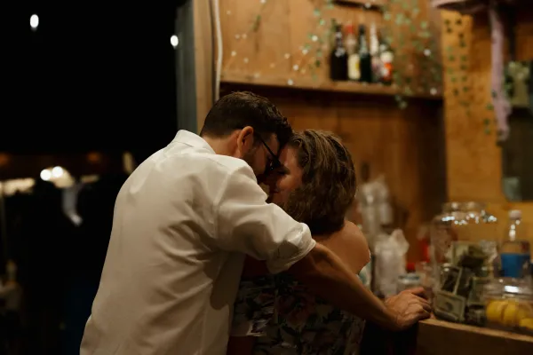 A couple in a close embrace, foreheads touching, at night. The man wears a white shirt, the woman a floral dress.