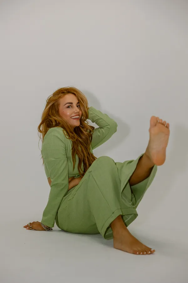 Smiling woman with long red hair in a light green two-piece outfit, sitting playfully on a white background, perfect for Charlotte NC branding photography.