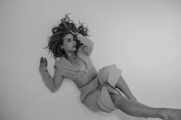 Black and white editorial photo of a woman in a stylish modern outfit, lying down with hair spread, looking confidently at the camera, perfect for branding.