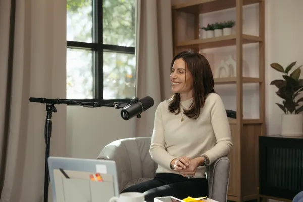 Smiling female podcaster in a modern studio setting with a microphone, laptop, and natural light, captured by a Charlotte NC branding photographer.