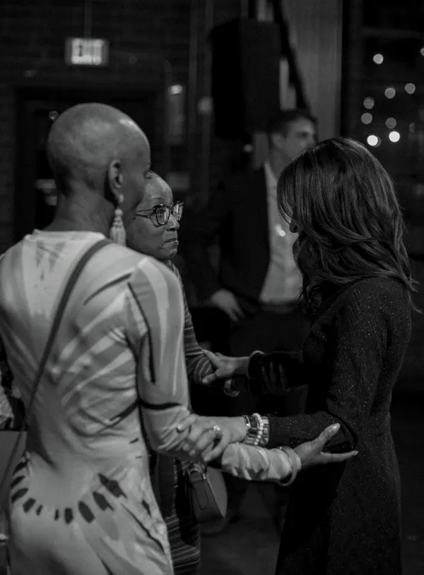 Black and white photo of three women networking and conversing at an event, with one woman in glasses looking engaged in conversation, and another woman's hands visible, showcasing bracelets.