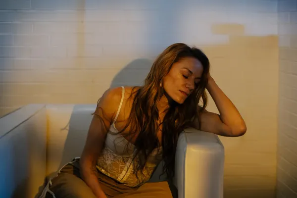 Woman with long brown hair, eyes closed, resting on a white sofa in warm golden hour light, suitable for Charlotte branding photography.