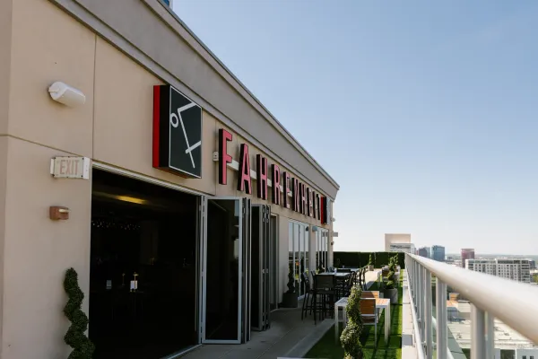 Exterior view of Fahrenheit Charlotte rooftop restaurant and bar with red signage, open doors, outdoor seating, and city skyline in the background on a sunny day.