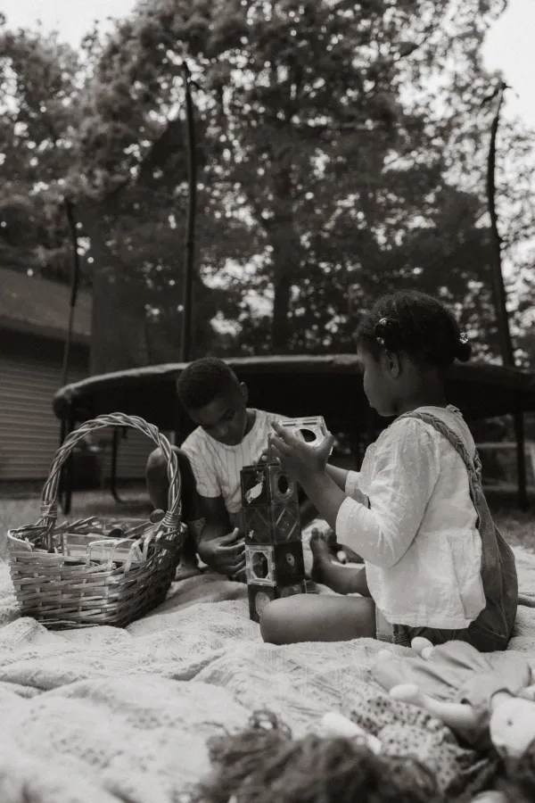 Two children playing with building blocks and a basket on a blanket outdoors in Charlotte, NC.