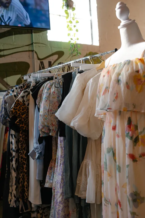 Colorful clothing on a rack with a floral dress on a mannequin in a bright Charlotte boutique.