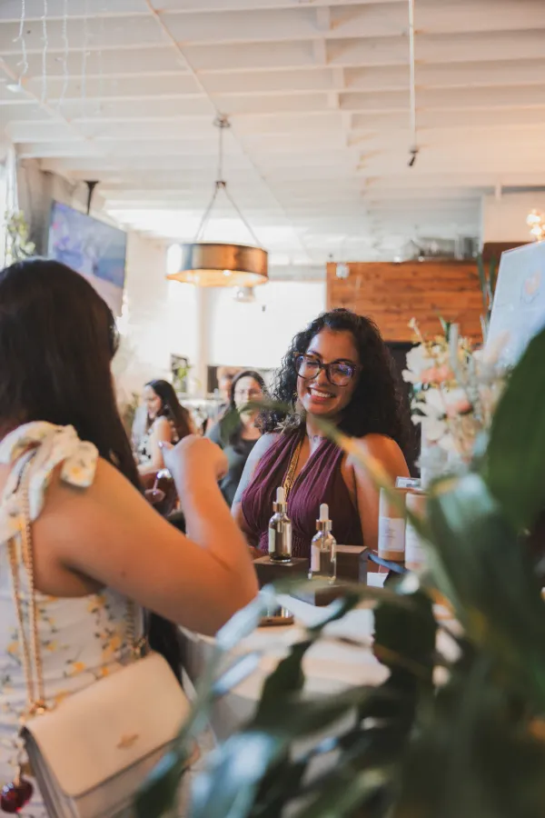 Two women smiling and interacting at a lively business event in Charlotte, NC, with product displays.