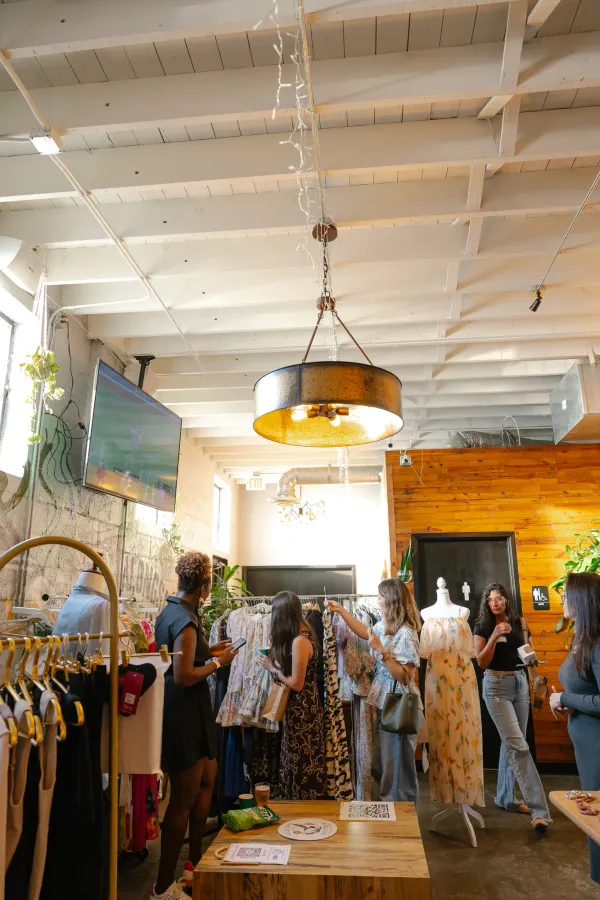 Women shopping for clothes at a lively boutique event in Charlotte, NC, with racks of colorful dresses.